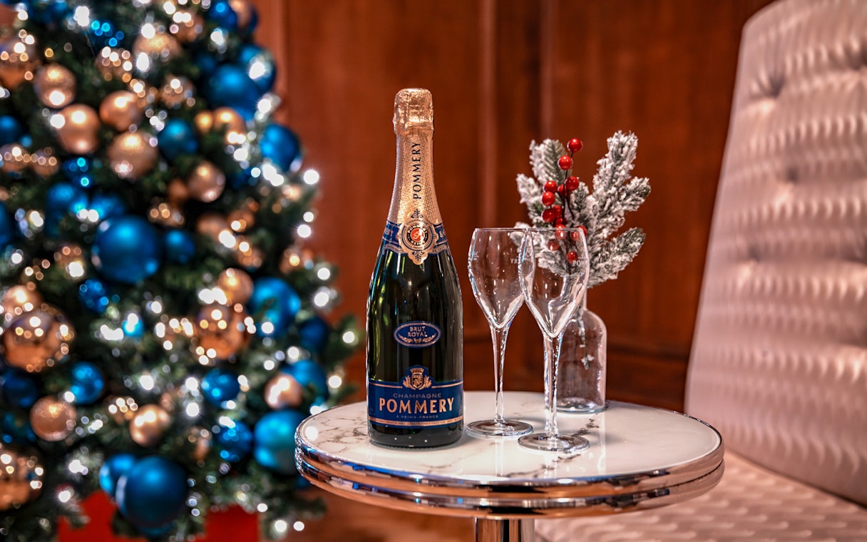 Champagne bottle and glasses on table with Christmas tree in background, London tour experience.