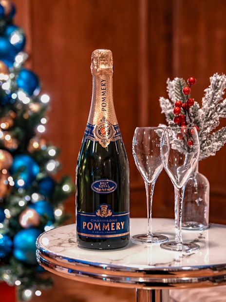 Champagne bottle and glasses on table with Christmas tree in background, London tour experience.