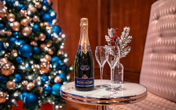 Champagne bottle and glasses on table with Christmas tree in background, London tour experience.