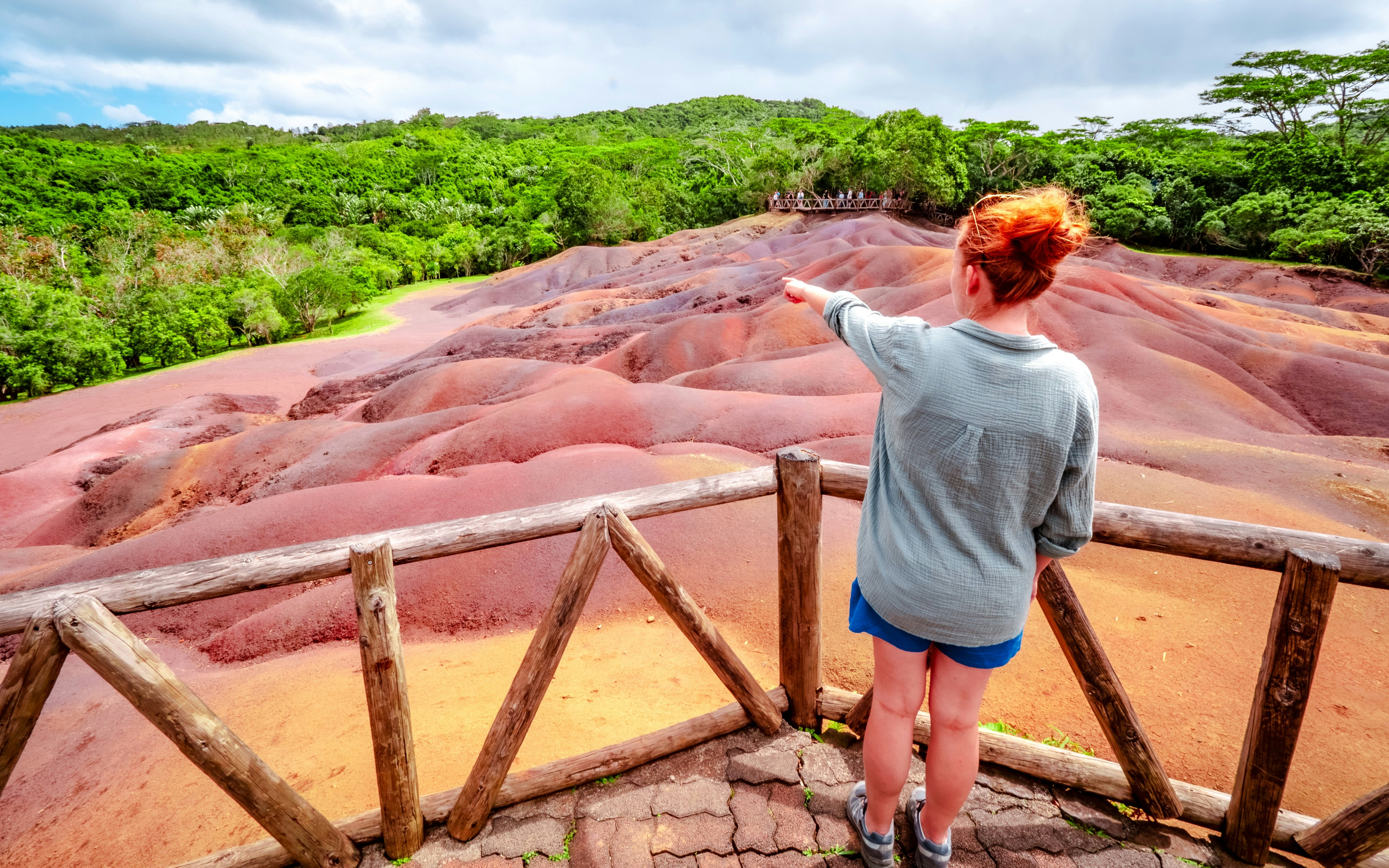 Visitor pointing at Chamarel 7 Coloured Earth in Mauritius with lush greenery in the background.