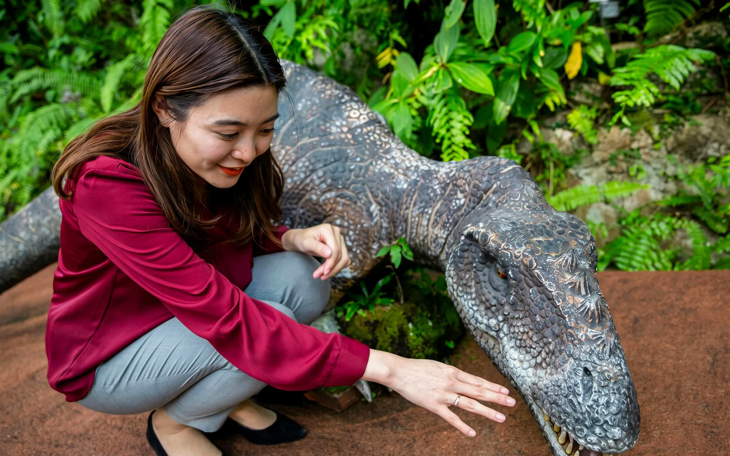 Visitor interacting with dinosaur sculpture at Okashigoten Nago Dino Park Yanbaru Subtropical Forest.