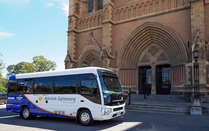 Adelaide sightseeing bus in front of historic cathedral entrance.