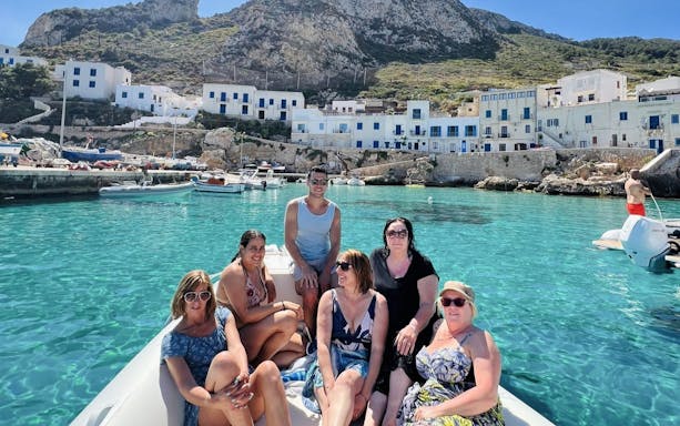 Boat tour group enjoying clear waters near Favignana with coastal village backdrop.