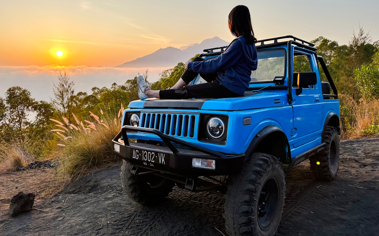 Person sitting on a blue jeep at sunrise during Black Lava Exploration in Bali.