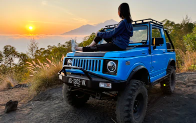 Person sitting on a blue jeep at sunrise during Black Lava Exploration in Bali.