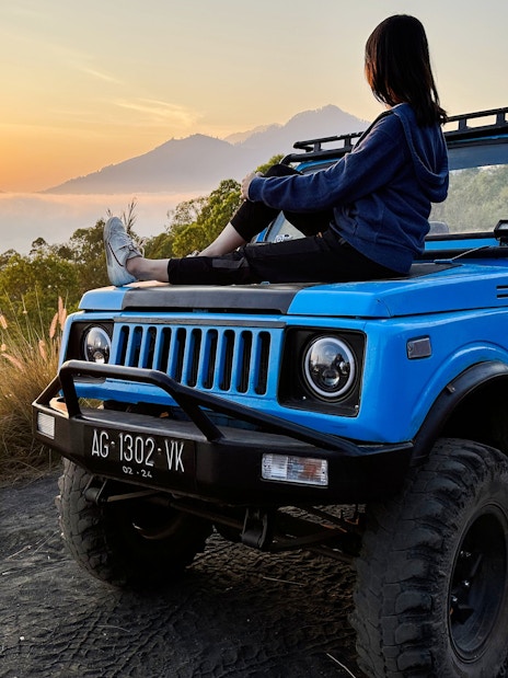 Person sitting on a blue jeep at sunrise during Black Lava Exploration in Bali.