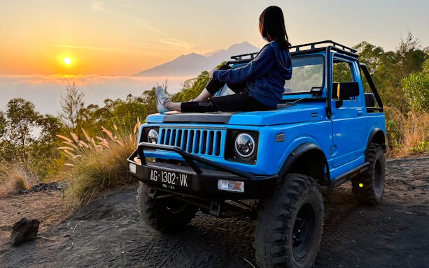 Person sitting on a blue jeep at sunrise during Black Lava Exploration in Bali.