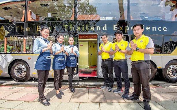 Staff welcoming guests on the Thai Bus Food Tour Experience in front of a tour bus.