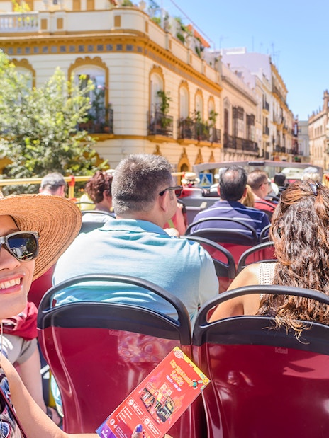 Tourists enjoying a City Sightseeing bus tour in Seville, passing historic buildings.