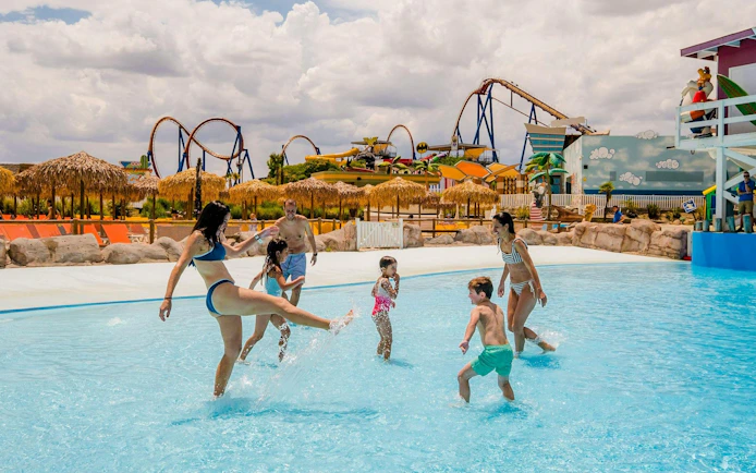 Families enjoying the wave pool at Parque Warner Beach with roller coasters in the background.