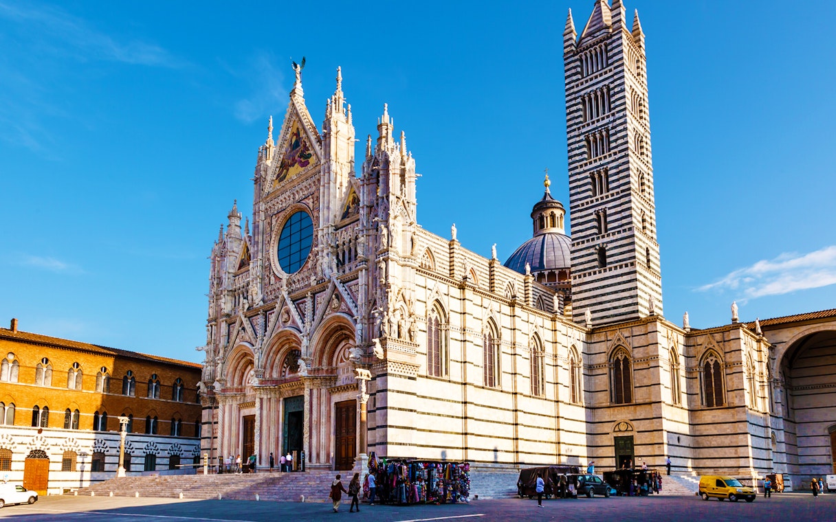 Siena Cathedral facade with bell tower under blue sky.