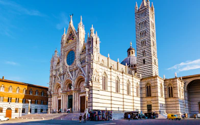 Siena Cathedral facade with bell tower under blue sky.