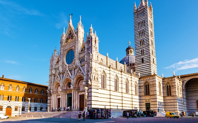 Siena Cathedral facade with bell tower under blue sky.