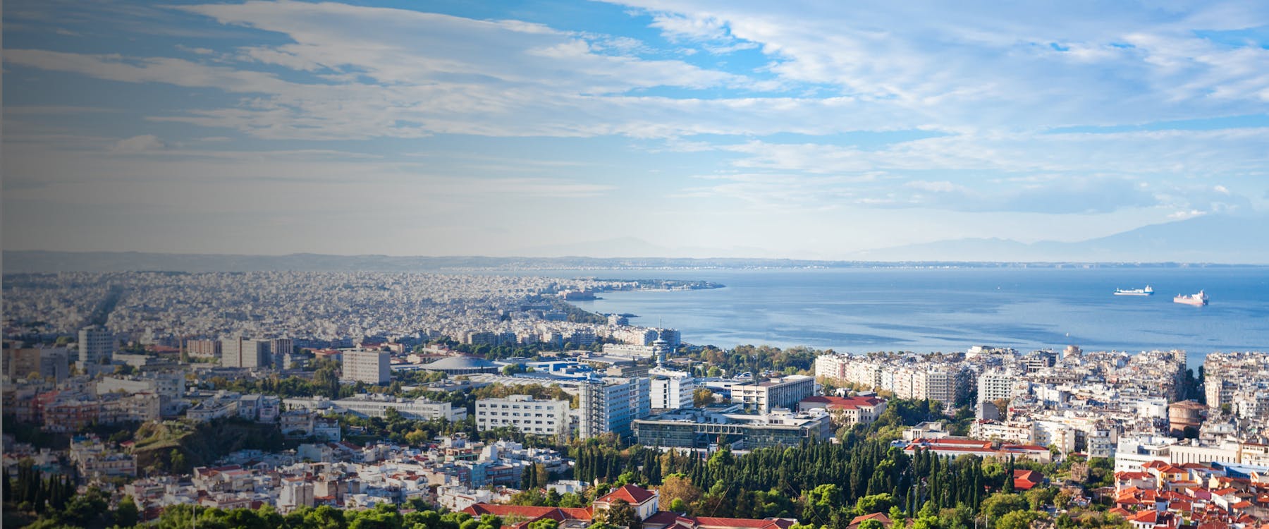 Aerial view of Thessaloniki cityscape with buildings and the Aegean Sea in the background.
