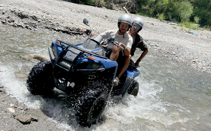 Two people riding a quad bike through a stream in Alcantara Gorges, Sicily.