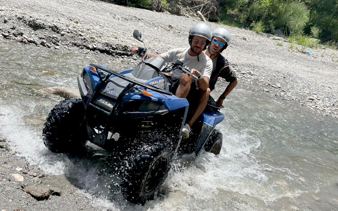 Two people riding a quad bike through a stream in Alcantara Gorges, Sicily.