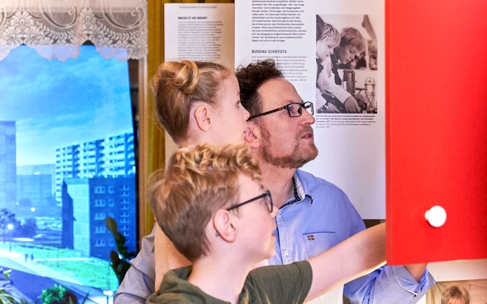 Father and kids exploring interactive exhibit at DDR Museum, Berlin.