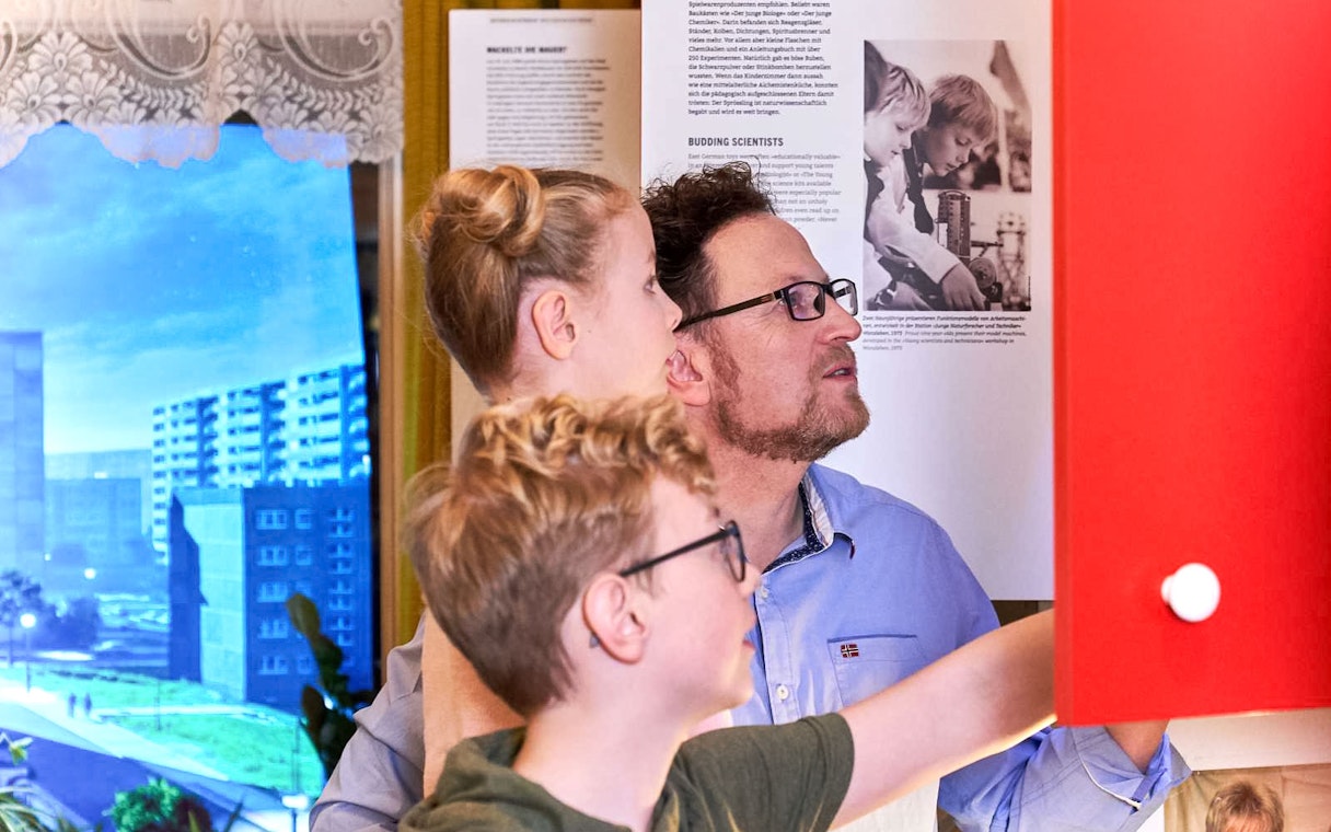 Father and kids exploring interactive exhibit at DDR Museum, Berlin.