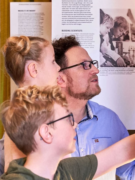 Father and kids exploring interactive exhibit at DDR Museum, Berlin.