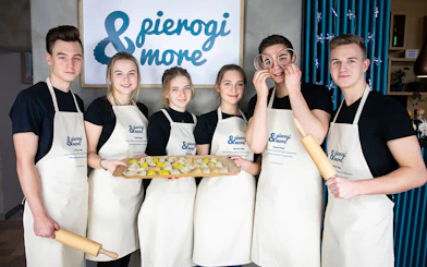 Group of people in aprons holding dumplings at a Polish cooking class.