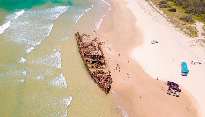 Aerial view of Maheno Shipwreck on Fraser Island's beach, K'gari, with tourists exploring.