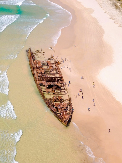 Aerial view of Maheno Shipwreck on Fraser Island's beach, K'gari, with tourists exploring.