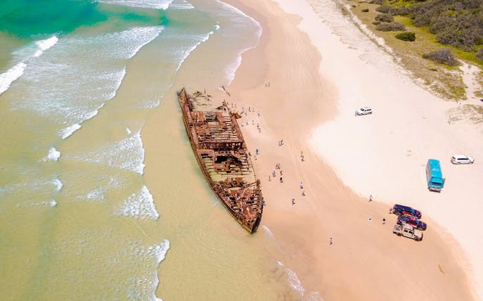 Aerial view of Maheno Shipwreck on Fraser Island's beach, K'gari, with tourists exploring.