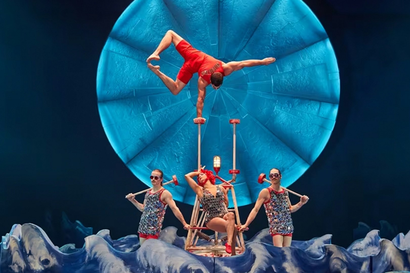 Acrobats performing a balancing act in Luzia show with a blue circular backdrop.