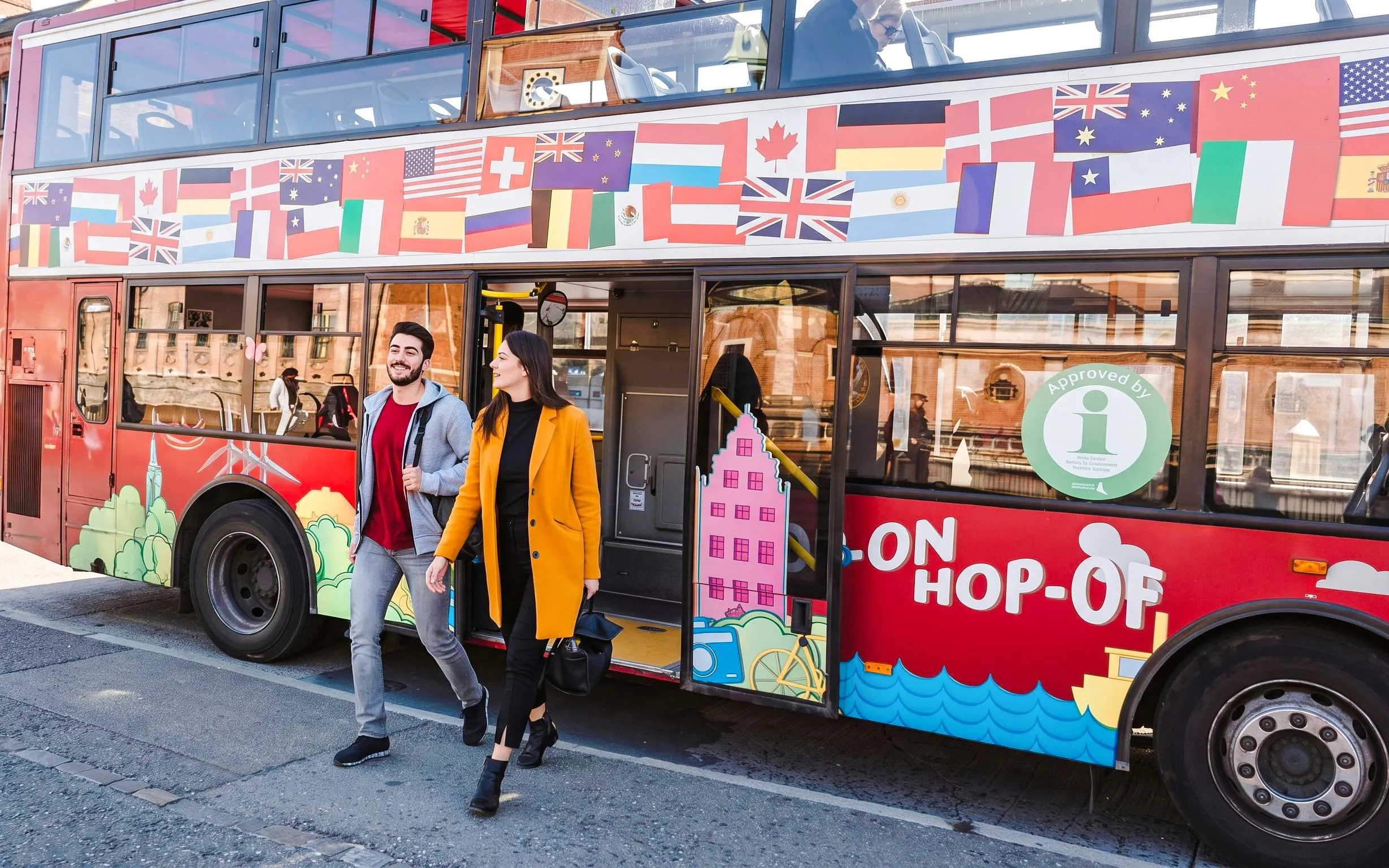 Guests exiting Copenhagen hop-on hop-off bus with colorful flags and cityscape design.