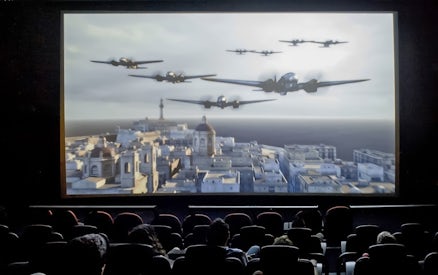 Audience watching Malta 5D show with planes flying over a cityscape.