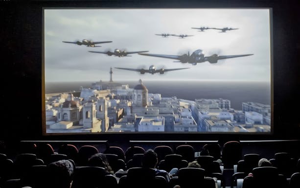 Audience watching Malta 5D show with planes flying over a cityscape.