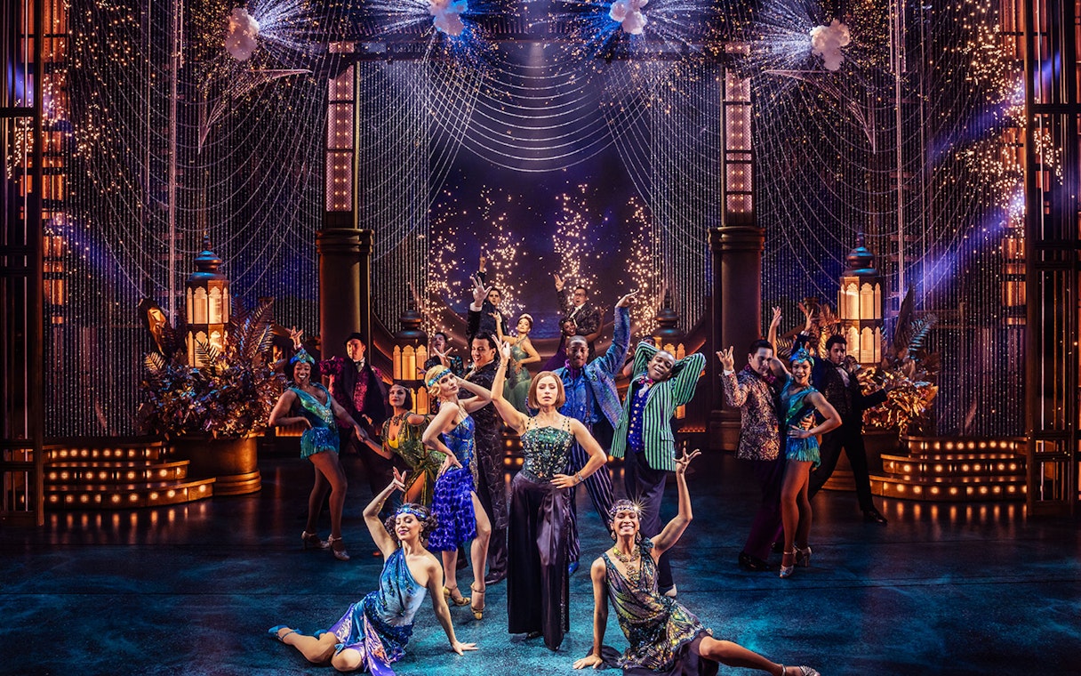Performers in a vibrant stage production of The Great Gatsby with fireworks and art deco set design.