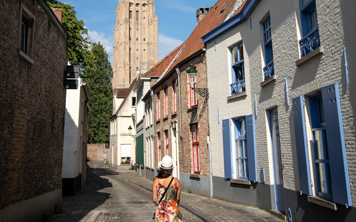 Woman walking on Stoofstraat toward Church of Our Lady, Bruges, Belgium.
