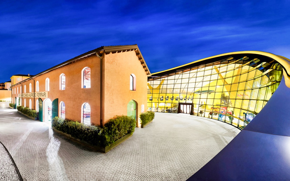 Museo Enzo Ferrari Modena entrance with modern glass facade at night.