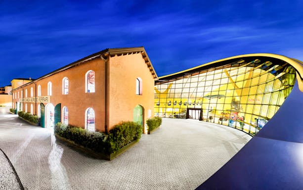 Museo Enzo Ferrari Modena entrance with modern glass facade at night.