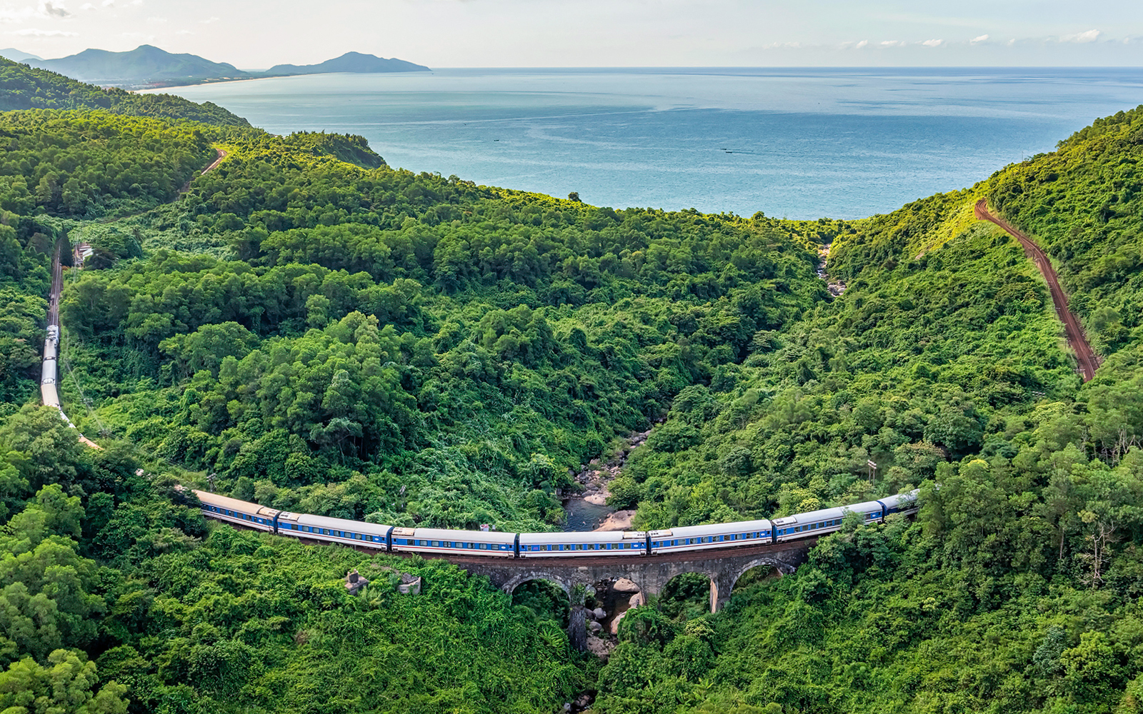 Aerial view of train crossing lush green Hai Van Pass, Vietnam.
