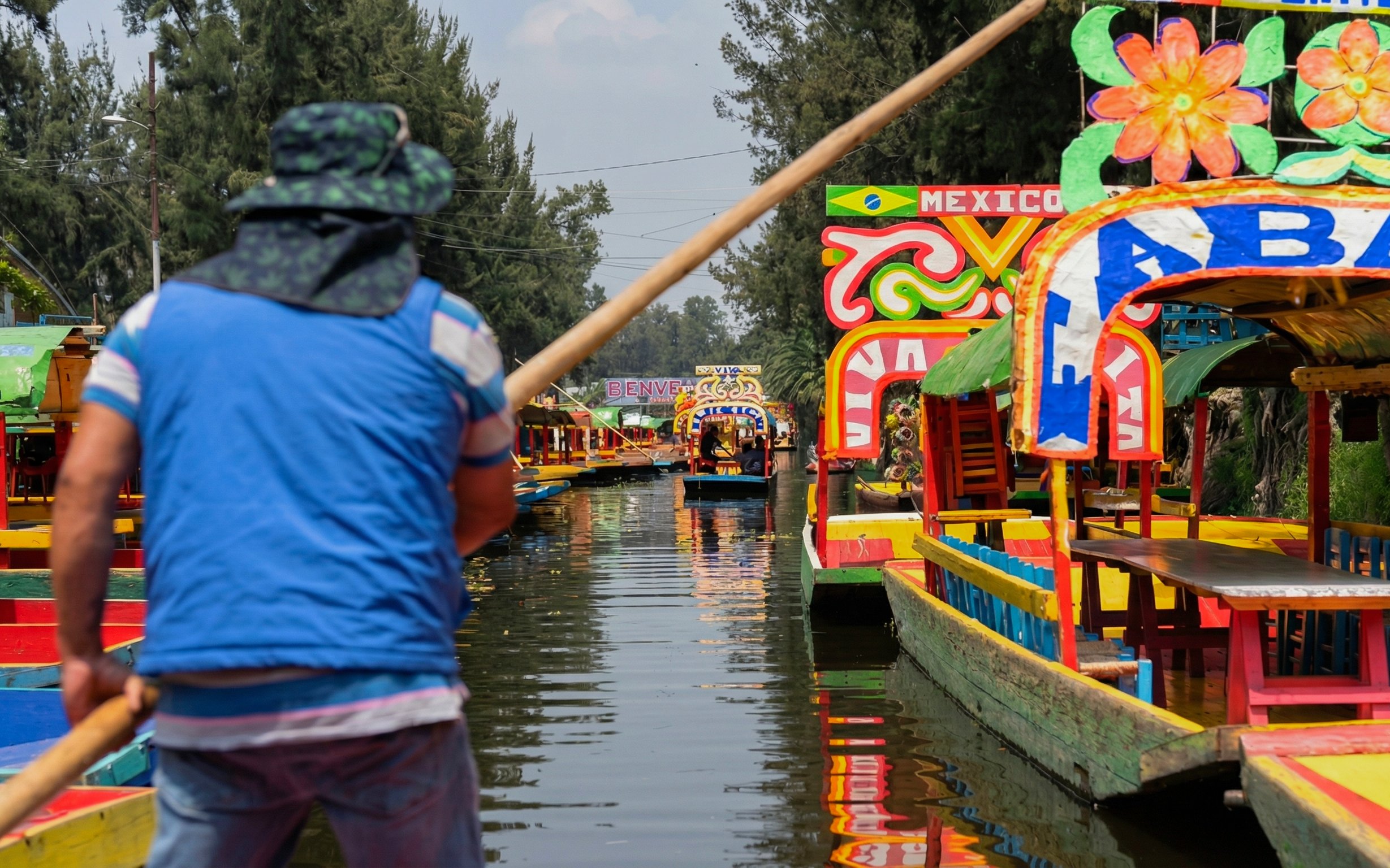 Colorful trajineras on Xochimilco canal with a guide steering the boat.