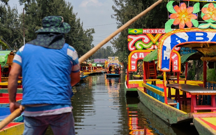 Colorful trajineras on Xochimilco canal with a guide steering the boat.