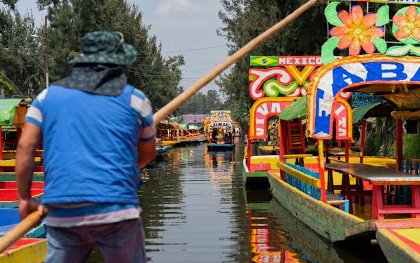 Colorful trajineras on Xochimilco canal with a guide steering the boat.