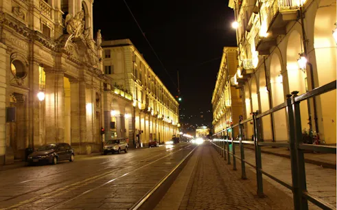 Night view of illuminated street and historic buildings in Turin, Italy.