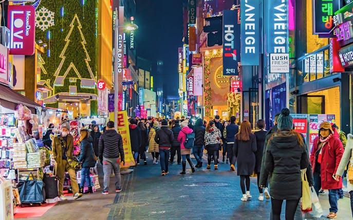 Crowded Myeongdong street in Seoul at night with bright neon signs.