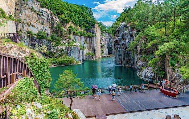 People on a pier viewing the lake at Pocheon Valley, Seoul, surrounded by cliffs and greenery.