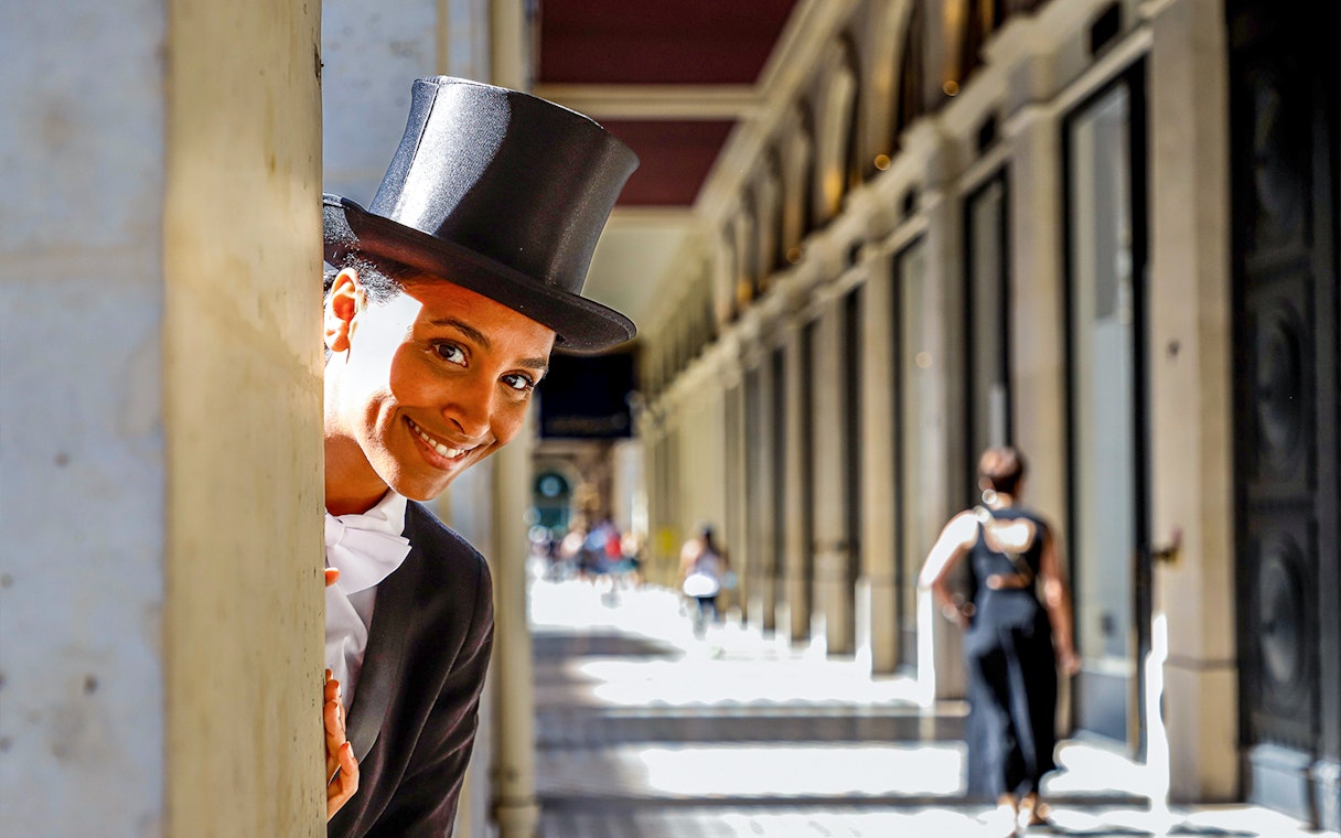Person in top hat peeking from column in Parisian arcade, part of Josephine Baker's Paris tour.