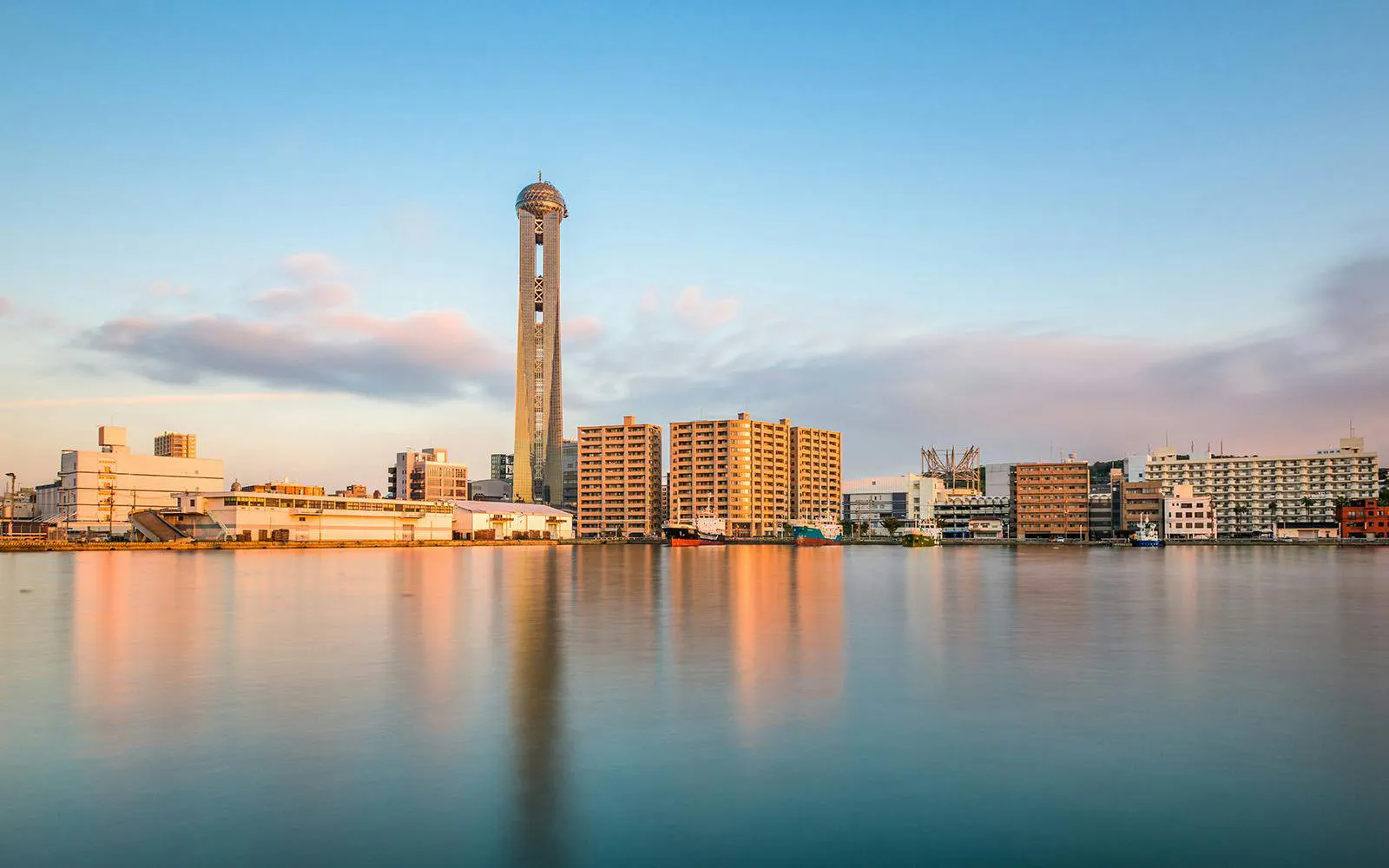 Shimonoseki waterfront skyline with Kaikyo Yume Tower and buildings reflecting on the water.