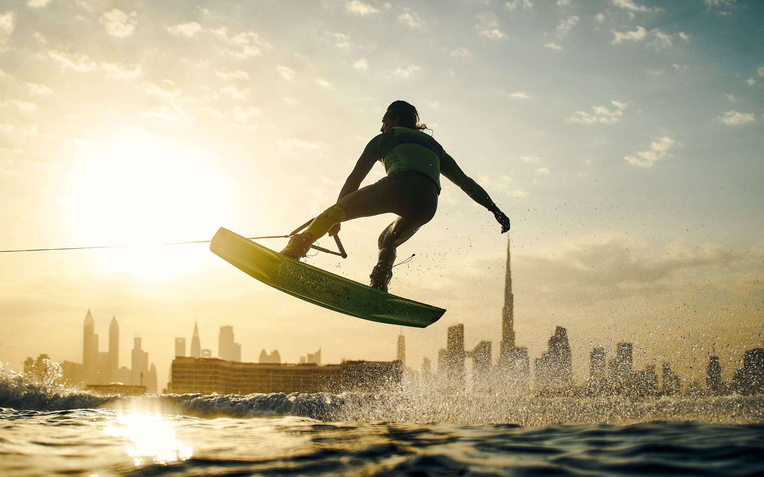 Tourist wakesurfing at sunset with Dubai skyline in background.