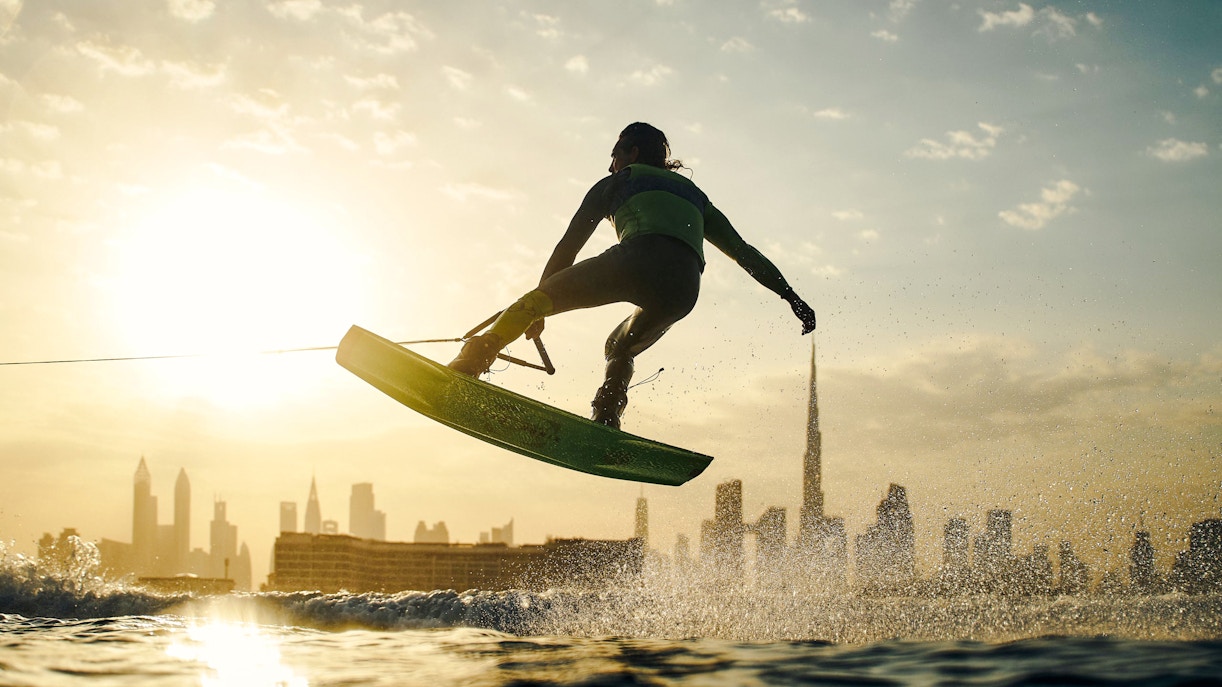 Tourist wakesurfing at sunset with Dubai skyline in background.