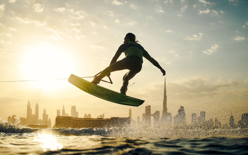 Tourist wakesurfing at sunset with Dubai skyline in background.