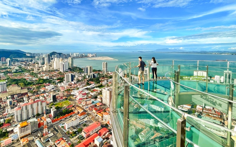 Couple enjoying the view from The Top, Penang's glass skywalk overlooking the city and sea.