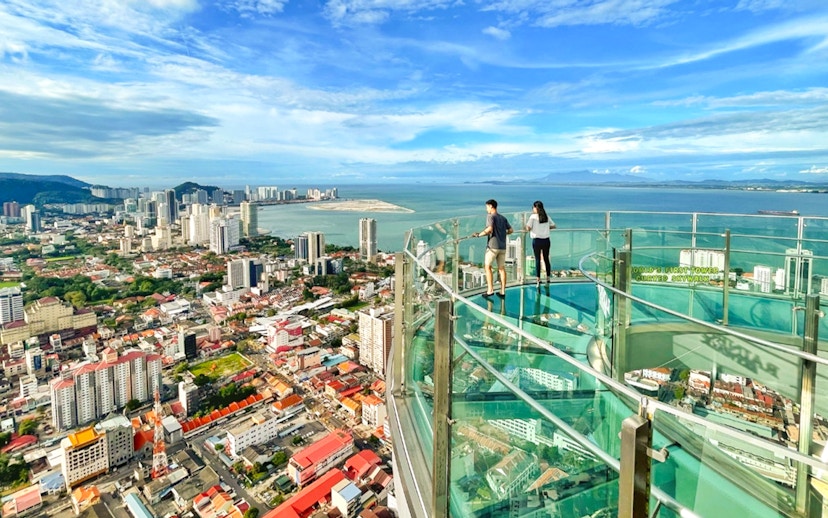 Couple enjoying the view from The Top, Penang's glass skywalk overlooking the city and sea.