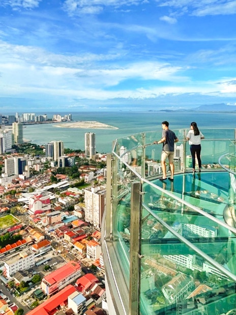 Couple enjoying the view from The Top, Penang's glass skywalk overlooking the city and sea.